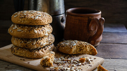 Oatmeal homemade cookies with grains on a wooden board, on the kitchen table and homemade coffee in a clay mug.