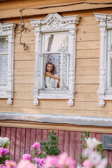 girl child in the window of a wooden house, carved platbands, village, summer