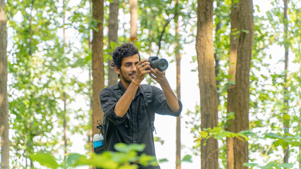 Young photographer standing in the nature, taking picture with professional camera