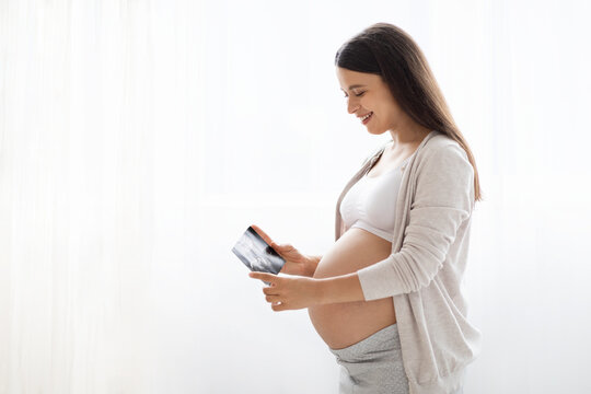 Cheerful pregnant woman holding ultrasound image, white background