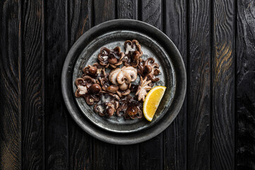 A dish of cooked baby octopus with a slice of lemon, shot from above, dark wooden backdrop