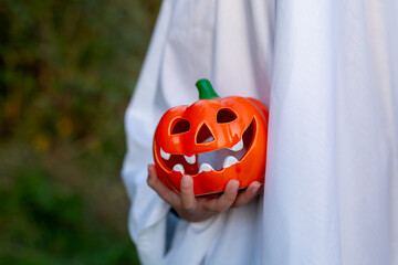 A bright orange pumpkin face in the hands of a child in a ghost costume