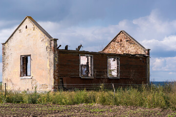 Stary,  zdewastowany i opuszczony dom pośród pól Świętokrzyskiego . Dom zbudowany z cegły kamienia i drewna . Na tle nieba i chmurek .