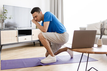 Fototapeta premium Fitness burnout. Exhausted arab man tired of online workout exercising at laptop sitting on fitness floor at home