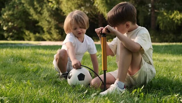 Two children of cheerful friends inflate a soccer ball with a pump.