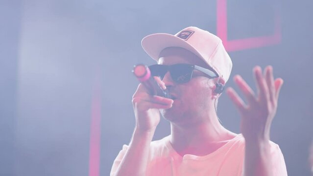 cool guy rapper with black sunglasses is performing on stage in music hall, concert of contemporary music