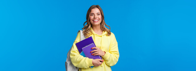 Cheerful pretty blond girl smiling at camera, carry backpack and notebooks, papers for studying,...