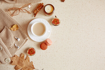 Fall lifestyle flat lay - casual sweater, woman glasess with headphones. Aesthetic coffee time among candle, fall leaves, macaroons cinnamon sticks. Copy space
