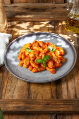 Close up of Italian potato Gnocchi with tomato sauce and fresh basil on gray plate on wooden background.