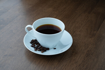 cup of black coffee with beans on a table with a wood texture