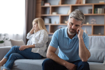 Boring sad mature caucasian male ignoring lady after quarrel and thinking about breaking up on sofa