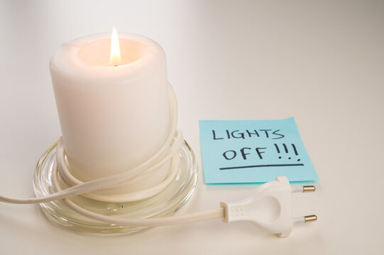 Lighted candle, electric plug, electric plug and card with "lights off" text. Energy savings, increased energy rates and bills.
