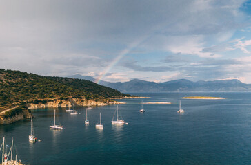 Naklejka na ściany i meble Sailboats anchored near coastline with rainbow in background