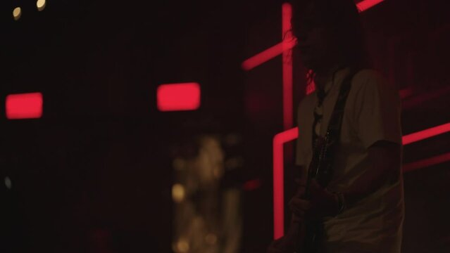 hard rock concert on stage, portrait of talented bass player with electric guitar in neon red lights