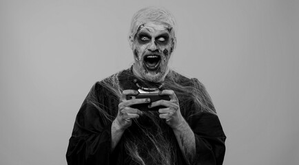 Spooky one man with horrible scary Halloween zombie makeup enthusiastically playing racing drive...