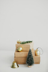Merry Christmas! Stylish eco christmas gift boxes on white table. Simple craft christmas presents with golden baubles, tree and fir branch on rustic wood. Eco friendly holiday banner