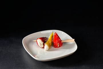 Finger food sticks with olives and stuffed pepperoni on white plate.