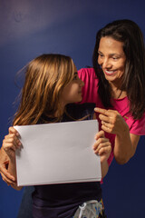 Mãe e filha abraçadas com cartaz em branco para reclame.
