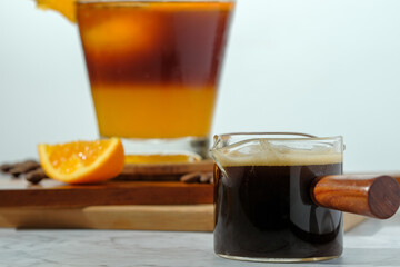 cold Iced black coffee mixed with orange juice and orange slices in glass on wooden plate in white background with nature leaves silhouette shadow. two tones layer fresh summer drink in the morning