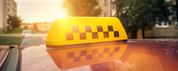 Yellow checkered taxi sign fixed on cab roof waiting for passenger at urban street close up view
