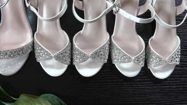 A row of identical women's, festive, white shoes with shiny stones stand on a black shelf. Beautiful new women's sandals with rhinestones are on the shelf in the store.