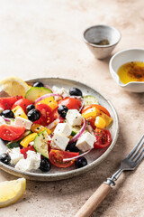 Vegetable greek salad with feta cheese, tomatoes, red onion, cucumber, pepper, olive oil and italian herbs served on brown background with rustic fork