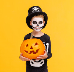 Happy cheerful boy in skeleton costume with  pumpkin  jack-o-lantern celebrates Halloween and...