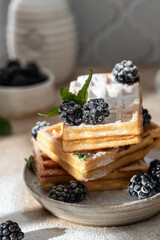 Stack of homemade belgium waffles close up with blackberry and powdered sugar on the kitchen table with tiles behind. Morning breakfast concept