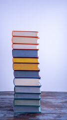 A high stack of used books in fabric bright multi-colored covers with textured paper cuts, on a vintage wooden table against a light background. Education, love of reading. Vertical orientation