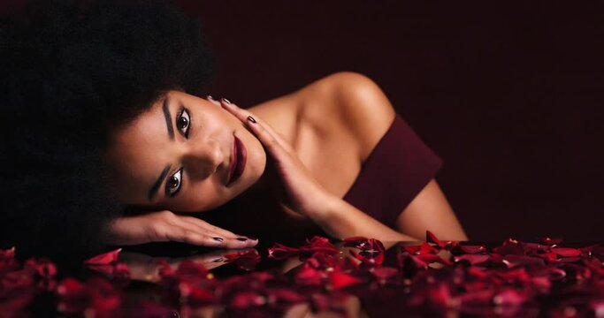 Sexy, seductive and black woman in petals from rose looking for love touching her face. Beauty, makeup and flowers, sensual lady from Brazil. Elegance, desire and flirt, Romance, red lips and roses.