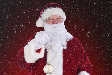 Closeup of Santa Claus holding a large gold pocket watch, on a light to dark red background with...