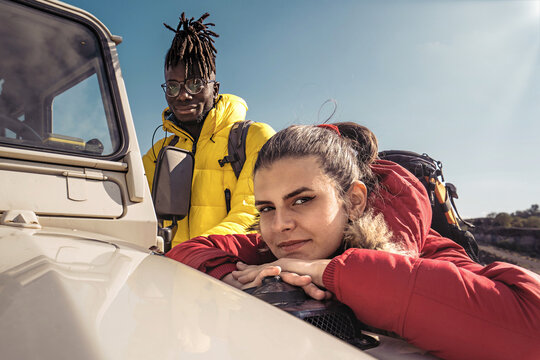 Multiethnic Couple Of Young Hikers With Backpack Of Young People Standing By An Off Road Vehicle