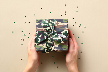 Female hands holding camouflage military gift box. Veterans Day holiday greeting card.