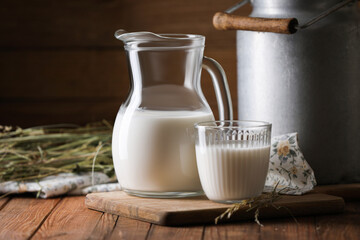 Tasty fresh milk in can, jug and glass on wooden table. Space for text