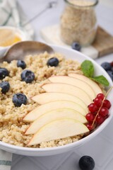 Bowl of delicious cooked quinoa with apples, blueberries and cranberries on white tiled table, closeup