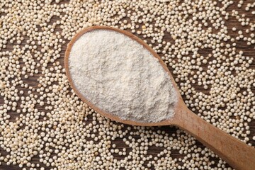 Spoon with quinoa flour and seeds on wooden table, top view
