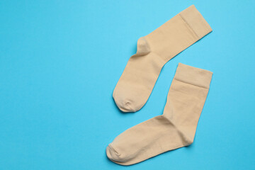 Beige socks on light blue background, flat lay. Space for text