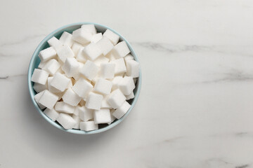 Fototapeta na wymiar Bowl of white sugar cubes on marble table, top view. Space for text