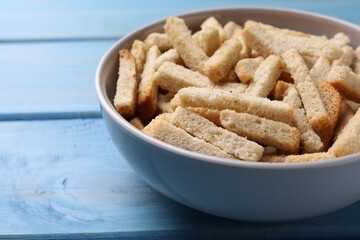 Crispy wheat rusks in bowl on light blue wooden table, closeup
