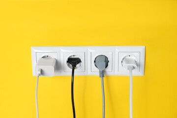Power sockets with inserted plugs on yellow wall. Electrical supply