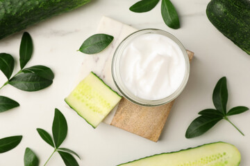 Obraz na płótnie Canvas Glass jar of cucumber face cream on white marble table, flat lay