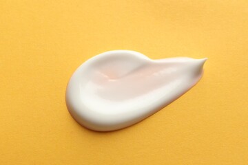 Sample of face cream on orange background, top view