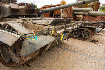 A destroyed military tanks with Ukrainian flags stands outdoors on the street. Destroyed. Army. Combat. Aggression. Burnt. Invasion. Machine. Attack. Conflict. Destruction. Tank. Broken. Equipment