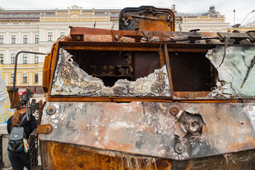 A destroyed military armored personnel carrier with destroyed armored windows stands outdoors on the street. Army. Combat. Aggression. Burnt. Invasion. Machine. Attack. Conflict. Destruction. Broken