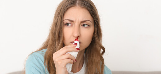 Young woman wiping nosebleed with tissue at home
