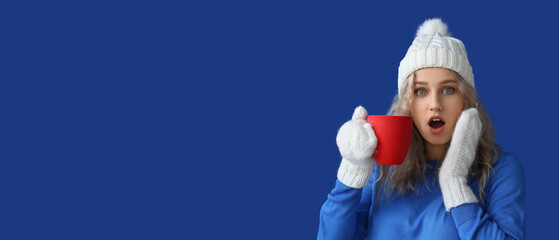 Surprised young woman drinking hot chocolate on blue background with space for text