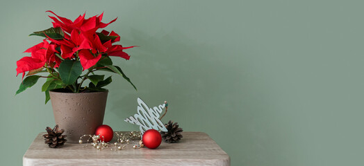 Beautiful poinsettia plant in pot with Christmas decorations on table against green background with space for text