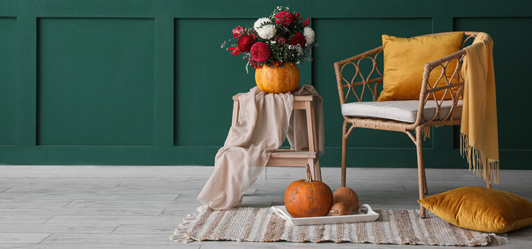 Wicker armchair with autumn pumpkins and beautiful bouquet of flowers near green wall in room