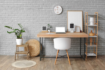 Interior of room with modern workplace and blank photo frames near grey brick wall