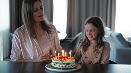 Happy single mother celebrating birthday with her little cute girl at home, having birthday cake with candles. Child kid girl blowing candles during birthday celebration. Fun event, family celebration